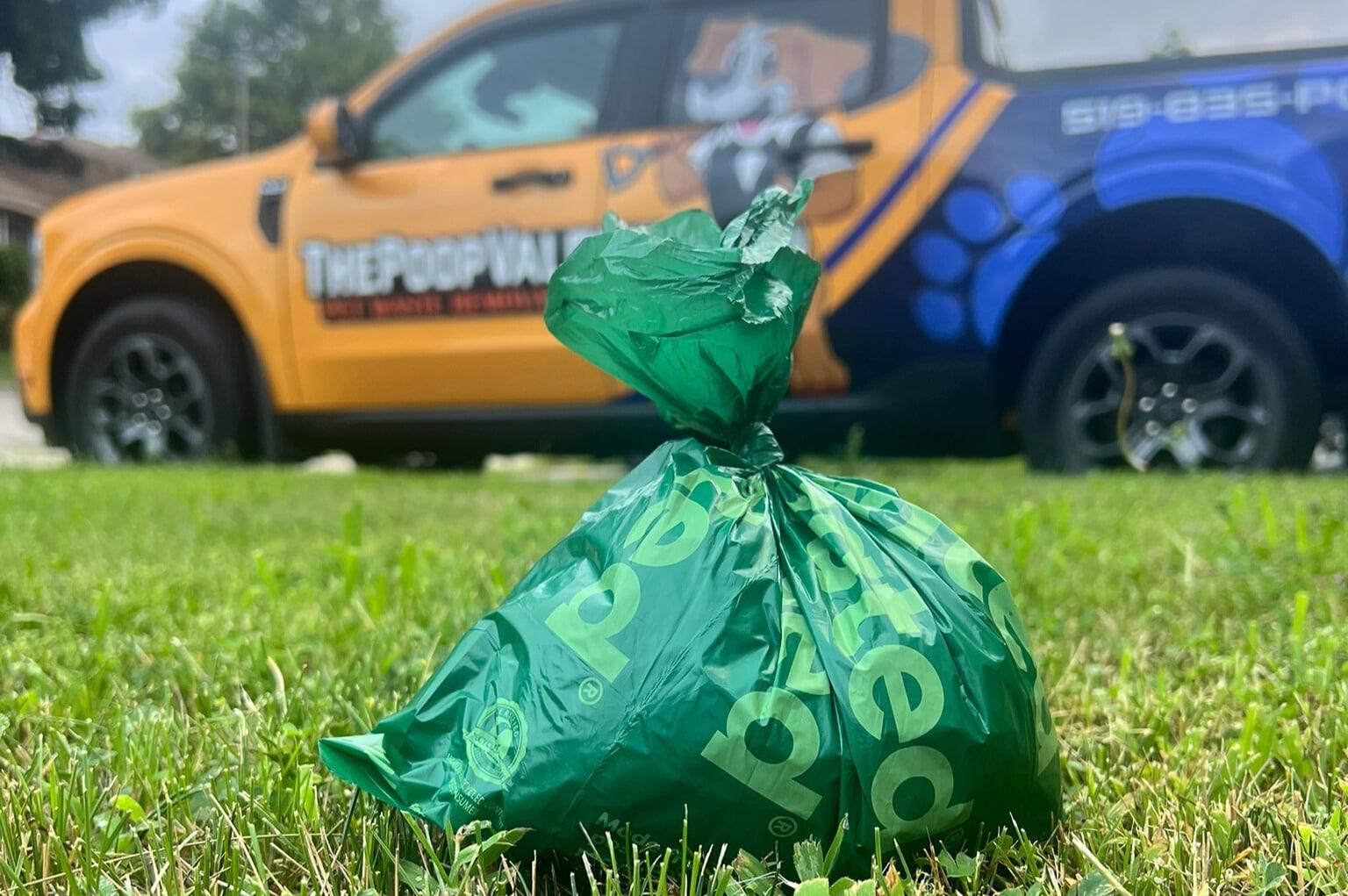Bagged dog waste collected during a weekly cleanup, with The Poop Valet service truck in the background